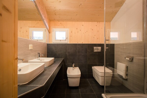 Een moderne badkamer met twee wastafels, toilet en douche.
