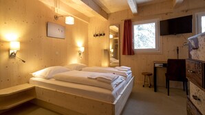 A wooden room with a bed, bedside tables, a desk, and a television. - Chalet # 20 with IR-sauna and whirlpool bath (Turrach)