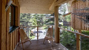 Een houten terras met twee houten stoelen en een kleine tafel, met uitzicht op een bebost gebied.