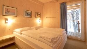 Een houten kamer met een bed, een raam met gordijnen en lijstjes met foto's aan de muur.