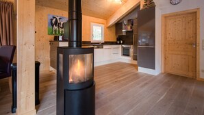 Een moderne keuken met een houtkachel, houten kasten en een eethoek met een stoel.