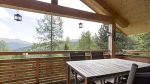 Eine Holzterrasse mit Tisch und Stühlen mit Blick auf eine gebirgige Landschaft.