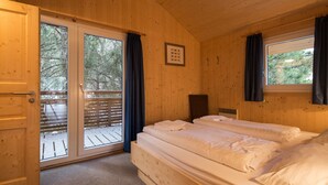 Camera da letto in una baita di legno con due letti, una porta scorrevole in vetro che dà su una terrazza e un quadro appeso al muro.