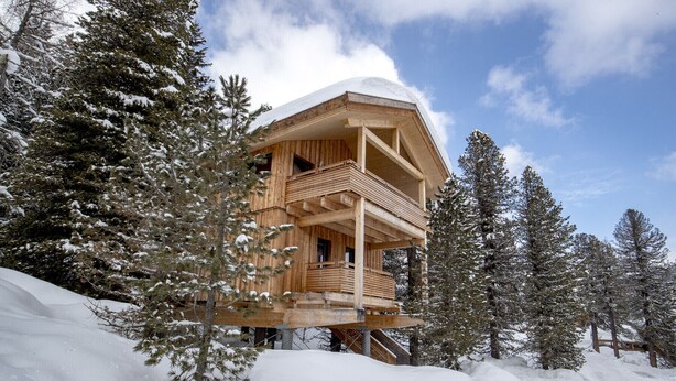 Una baita di legno con un balcone, circondata da alberi innevati.