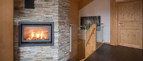 A stone fireplace with a glass front, a wooden door, and a glass partition in a room with dark flooring.