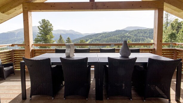 Um deck de madeira com mesa e cadeiras, com vista para uma paisagem montanhosa.