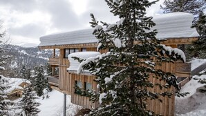 Uma cabana de madeira com varanda, rodeada por árvores e montanhas cobertas de neve.