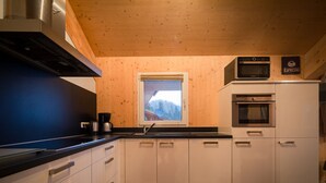 Uma cozinha moderna com armários brancos, bancada preta, micro-ondas embutido e janela com vista para uma montanha.