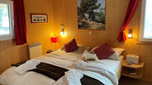 A wooden-paneled room with a large bed, red curtains, a framed picture, and a nightstand with a lamp. - Chalet #40 with IR-sauna and indoor whirlpool (Turrach)
