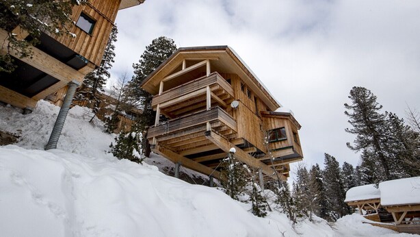 A wooden chalet with a balcony, surrounded by snow-covered trees. - Chalet #40 with IR-sauna and indoor whirlpool (Turrach)