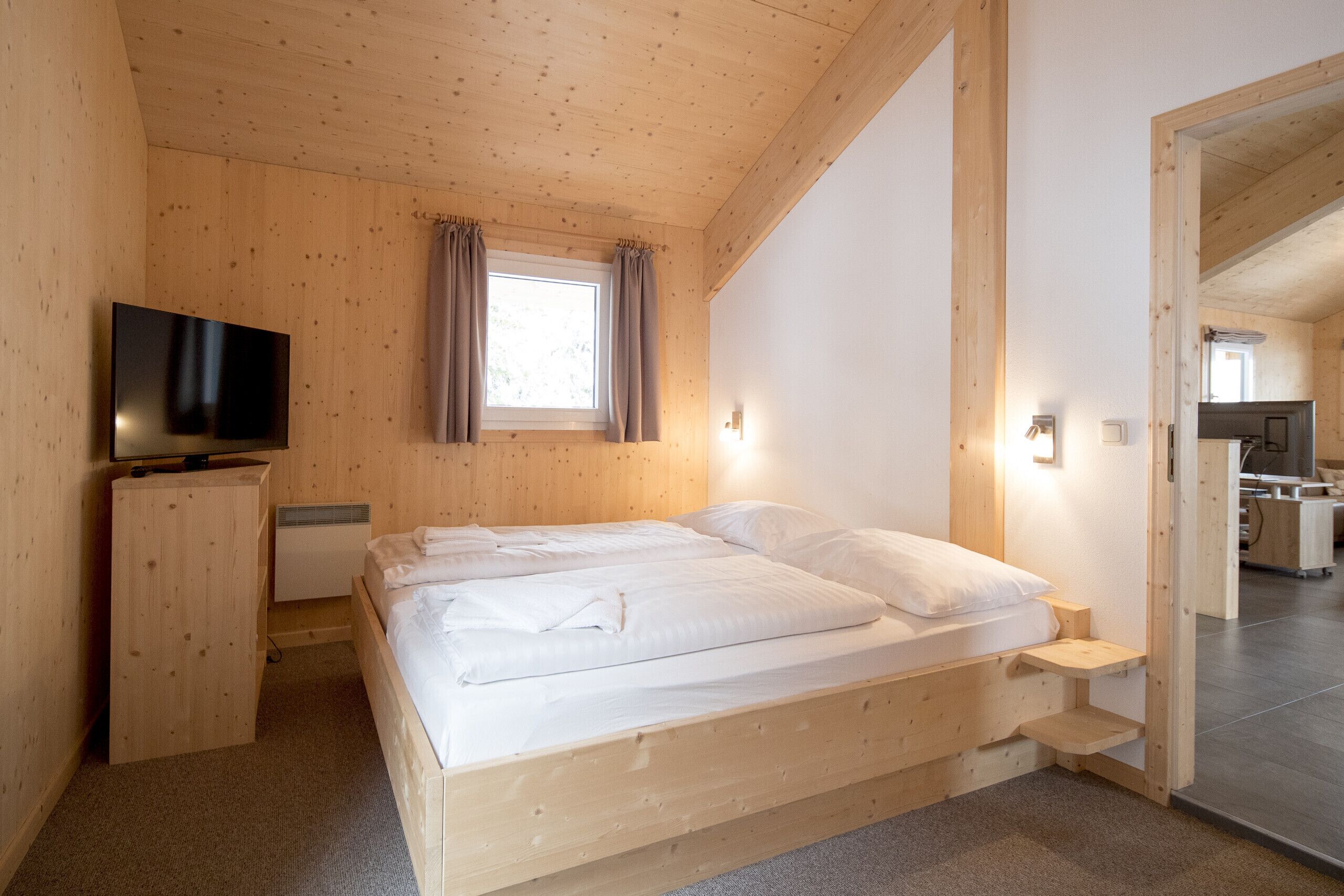A wooden-paneled bedroom with a bed, a TV, and a window with curtains.