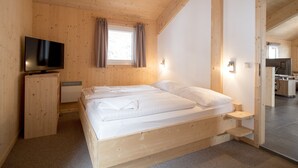 Une chambre aux murs lambrissés, avec un lit, une télévision et une fenêtre avec des rideaux.