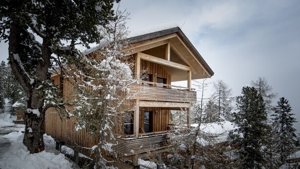 Une cabane en bois dotée d’un balcon, entourée d’arbres couverts de neige.