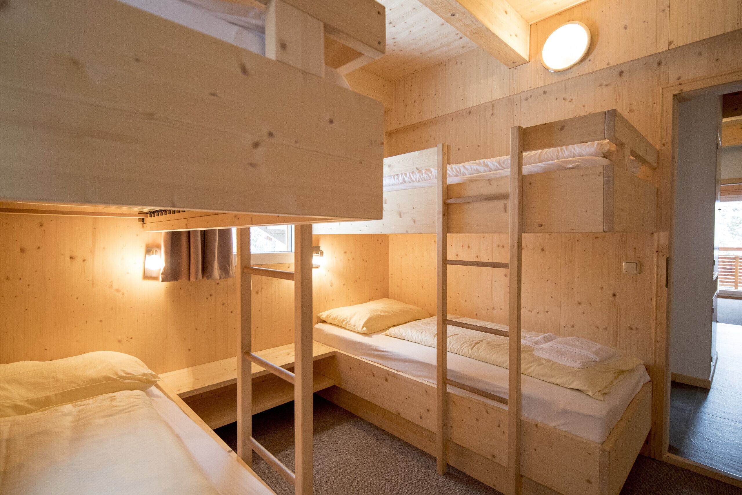 Een houten hut met stapelbedden, een klein raam en een deur die naar buiten leidt.