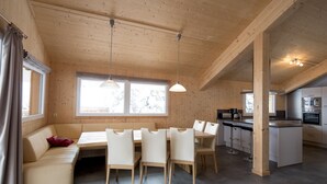 Une cuisine moderne avec des meubles en bois, un coin repas comprenant un banc et des chaises, et de grandes fenêtres qui laissent entrer la lumière naturelle.