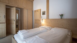 Een houten kamer met twee bedden, een houten kledingkast en een klein wandplankje met een vaas.
