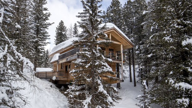 Een houten chalet met een balkon, omringd door met sneeuw bedekte bomen.