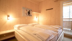 Une pièce en bois avec un lit, deux lampes fixées au mur et une fenêtre avec des stores.