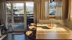 Un interior de madera con comedor, puertas de vidrio correderas que dan a una terraza exterior y vistas a un paisaje nevado.