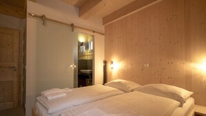 A hotel room with a wooden ceiling, a bed with white linens, a wooden wardrobe, and a mirror.