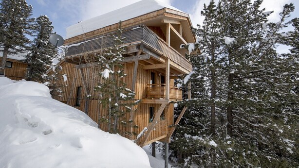 A wooden cabin with a balcony, surrounded by snow-covered trees.