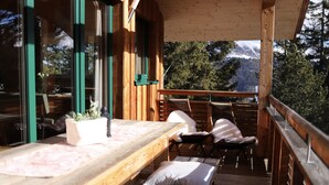 A wooden deck with a table and chairs, overlooking a mountainous landscape.