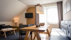 A modern living room with a wooden dining table, black leather sofa, and a mounted flat-screen TV. - Apartment # 12 with balcony (Turrach)