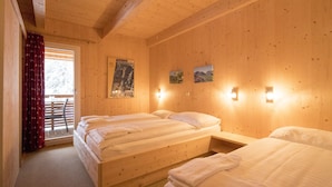 Une chambre d’hôtel avec trois lits en bois, un balcon avec des rideaux rouges et des lampes fixées au mur.