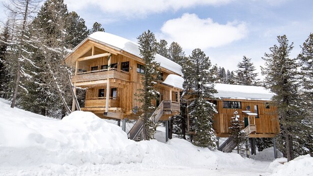 Un chalet en bois doté d’un balcon, entouré d’arbres couverts de neige.