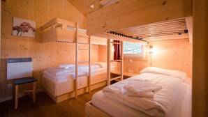 Une chambre dans un chalet en bois, avec des lits superposés, un bureau et une fenêtre.