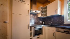 Une cuisine compacte dotée d’appareils électroménagers intégrés, de meubles de rangement en bois et d’une fenêtre laissant entrer la lumière naturelle.
