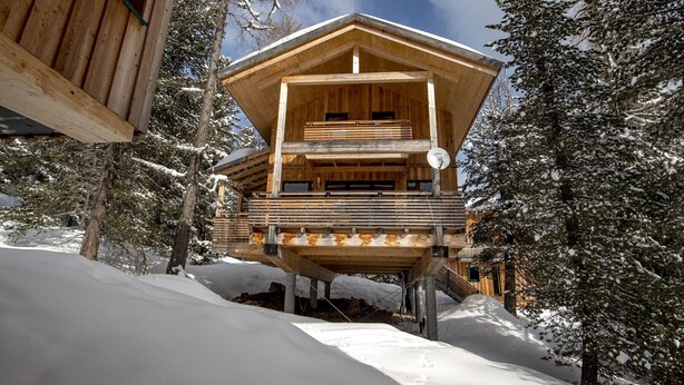 Une cabane en bois dotée d’un balcon, entourée d’arbres couverts de neige.
