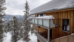 Een houten chalet met een balkon dat uitkijkt op een besneeuwd berglandschap.