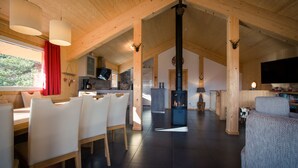 Een ruime woonkamer met een hoge nok, houten balken, een open haard en een televisietoestel.