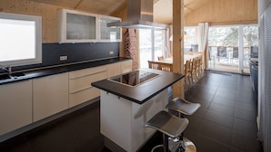 A modern kitchen with a central island, wooden cabinets, and a large window. - Chalet #26 with IR-sauna and indoor whirlpool (Turrach)