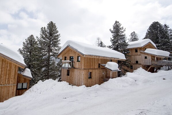 Houten hutten met sneeuwbedekte daken, omgeven door sneeuw en bomen.