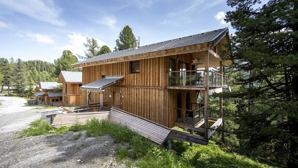 A wooden cabin with a balcony and a covered porch, surrounded by forest. - Chalet #26 with IR-sauna and indoor whirlpool (Turrach)