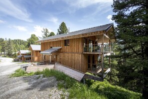 Une cabane en bois dotée d’un balcon et d’une véranda couverte, entourée de forêt.