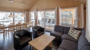 A cozy interior with a wooden ceiling, a sofa, a table, and chairs. Large windows offer a view of the outdoors. - Chalet #26 with IR-sauna and indoor whirlpool (Turrach)