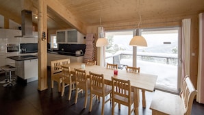 A wooden interior with a kitchen, dining area, and large windows. - Chalet #26 with IR-sauna and indoor whirlpool (Turrach)