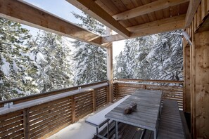 Een houten terras met een tafel en banken, omgeven door met sneeuw bedekte bomen.