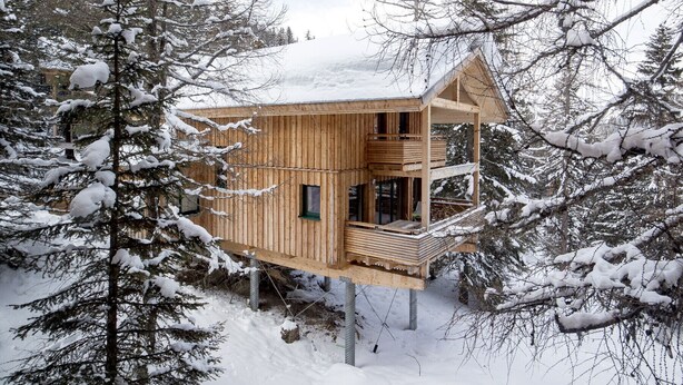 Eine Holzblockhütte mit Balkon, umgeben von schneebedeckten Bäumen.