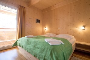Una habitación con paneles de madera, una cama, dos luces fijadas a la pared y un ventanal con cortinas.