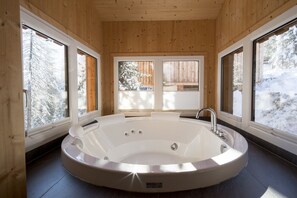 Un baño moderno con una bañera independiente grande, paredes de madera y amplias ventanas con vistas a un paisaje nevado.