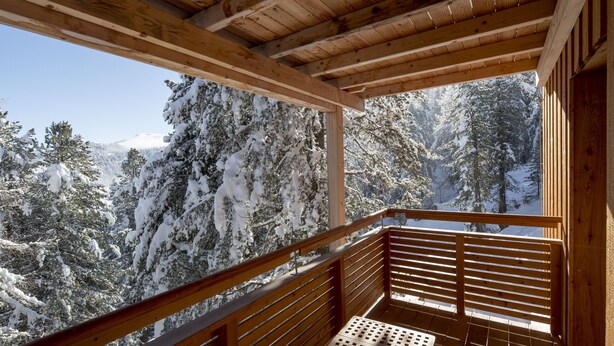 A wooden balcony with a table and bench, overlooking a snowy forest.
