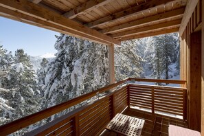 Ein Holzbalkon mit Tisch und Bank, mit Blick auf einen verschneiten Wald.
