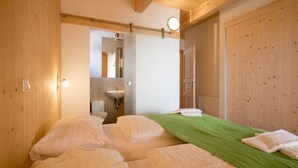 A bedroom with two beds, a green bedspread, white pillows, a wooden door, and a bathroom visible through an open door.