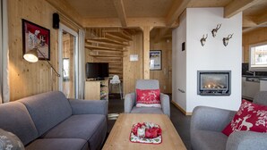 A cozy living room with a fireplace, wooden walls, and a television. - Chalet #30 with IR-sauna and indoor whirlpool (Turrach)