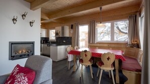 A cozy cabin interior with a fireplace, wooden dining table, and chairs. - Chalet #30 with IR-sauna and indoor whirlpool (Turrach)
