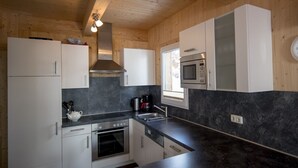 A compact kitchen with white cabinets, a black countertop, a stove, an oven, a microwave, and a window. - Chalet #30 with IR-sauna and indoor whirlpool (Turrach)